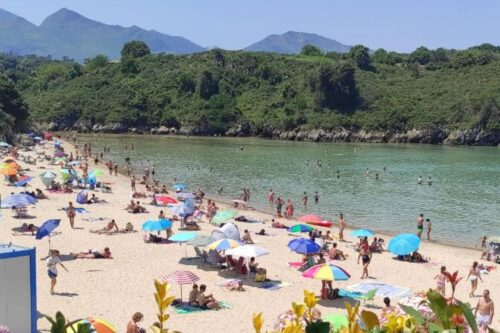 Playa de Poo con bañistas disfrutando del sol y el baño en el mar Cantábrico.